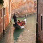 photo of a gondola in a canal between red brick buildings in venice italy