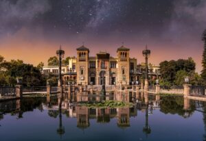 an image of a park in seville spain with a building and pond at night