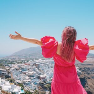 photo of a woman in a pink dress looking down at the city of Santorini in greece