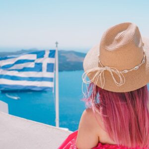 photo of woman in pink dress overlooking ocean with greek flag in santorini