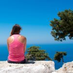 photo of woman sitting on a stone wall looking at ocean