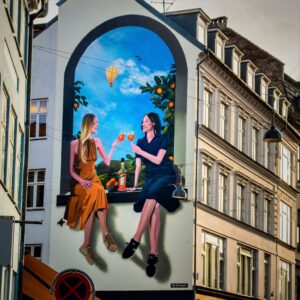 photo of a mural on the side of a building of two women drinking orange juice