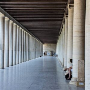 photo of a man sitting in a hallway of columns in athens greece