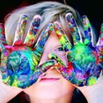photo of a child holding paint covered hands over his face