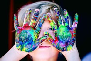 photo of a child holding paint covered hands over his face