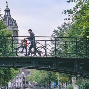 photo of a man pushing a bike over a bridge in amsterdam netherlands