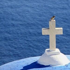 photo of a white cross with bird on it with ocean in santorini