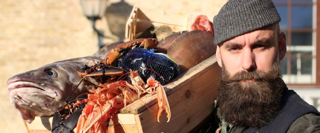 photo of a bearded man holding a box of fish on his shoulder