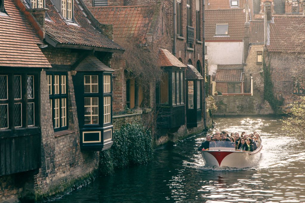 photo of a tourist boat passing building in a canal in bruges belgium
