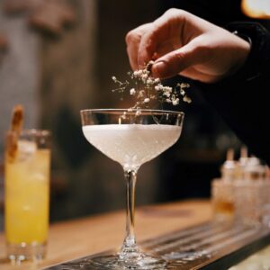 photo of a hand adding a garnish to a white cocktail in a bar