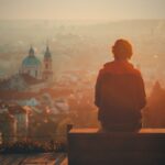 photo of a seated man looking over the city of prague at sunrise